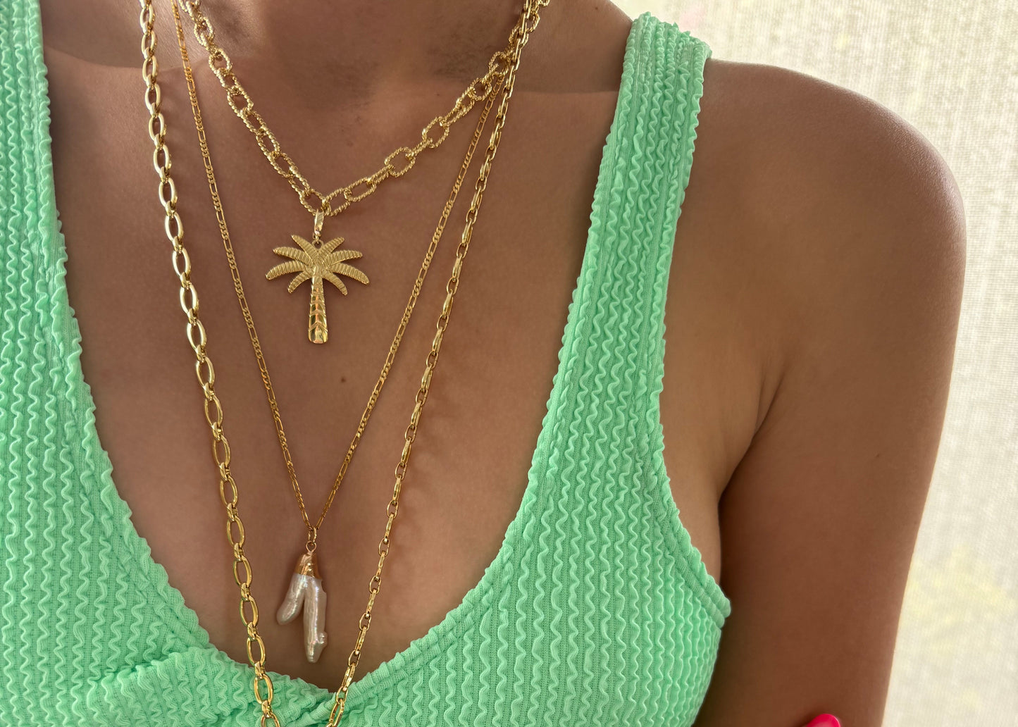 Person wearing a green bikini with gold jewelry on a neutral background