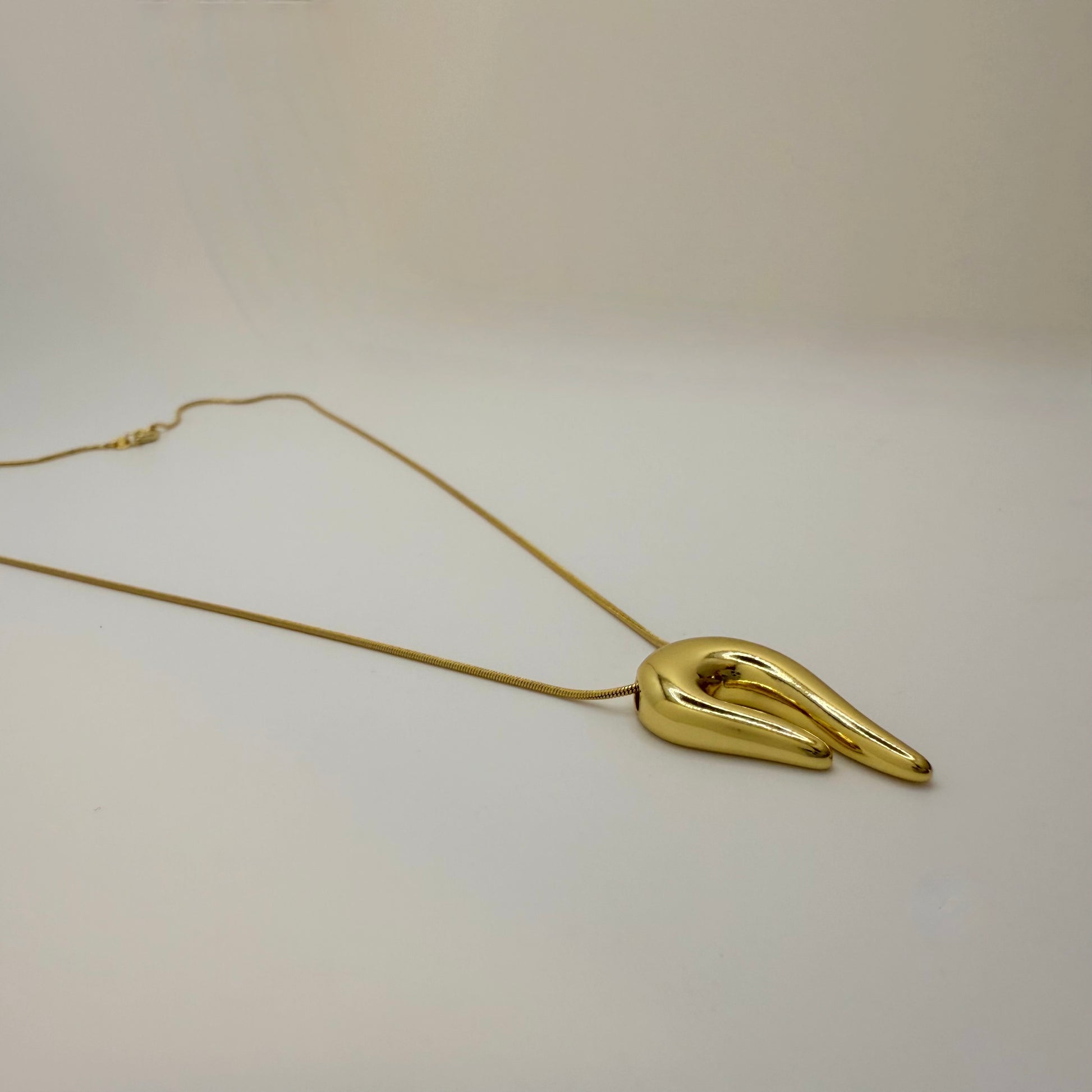 Gold necklace with a unique pendant on a light beige background